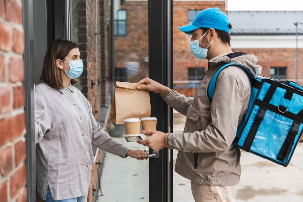 Delivery agent handing food and beverages to a customer at the door.