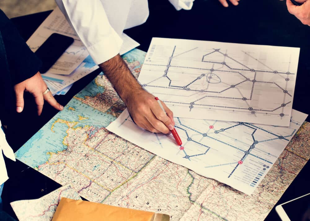 Team analyzing logistics routes on printed maps with a smartphone and documents on the table.