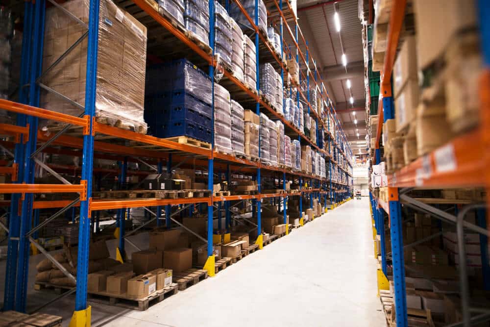 Interior view of a large warehouse with high shelves stacked with goods and cardboard boxes.